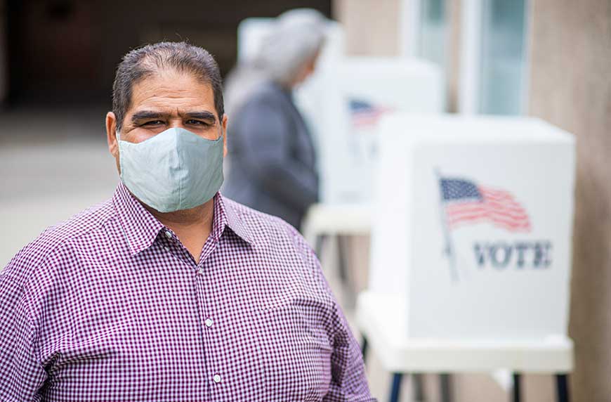 Man in mask at voting station wondering how the 2020 election could affect healthcare