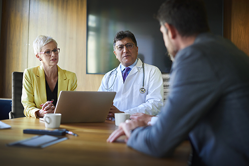 Physician sits at table with two hospital administrators